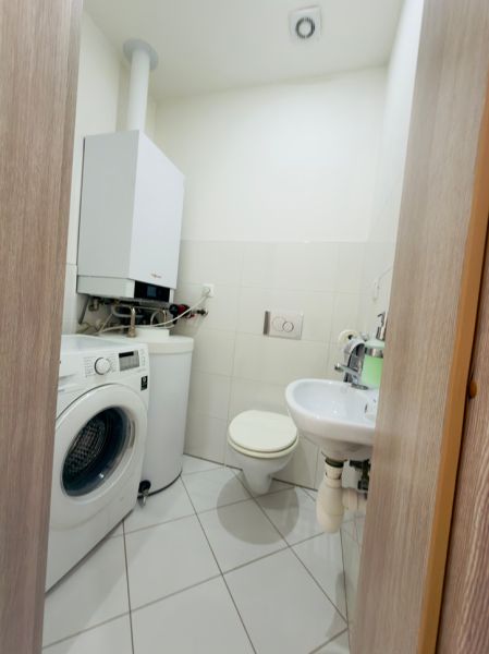A bathroom in a family house with a boiler, washing machine, and sanitary facilities on tiles.