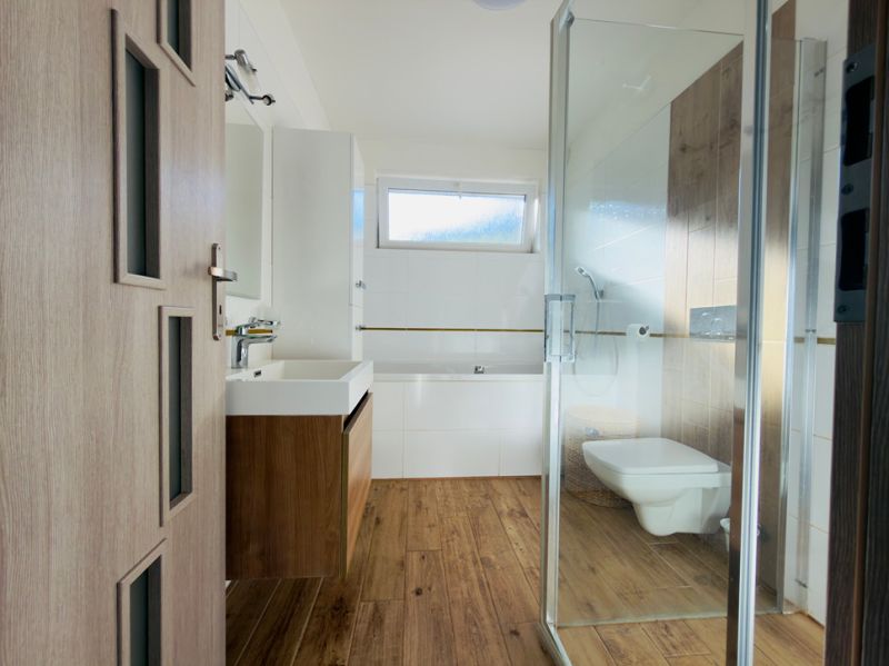A bathroom with a wooden decor floor in a family house with a sink and a shower.