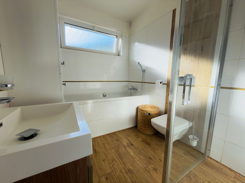 A bathroom in a family house with a bathtub, a shower corner, and a floor with a wooden decor.