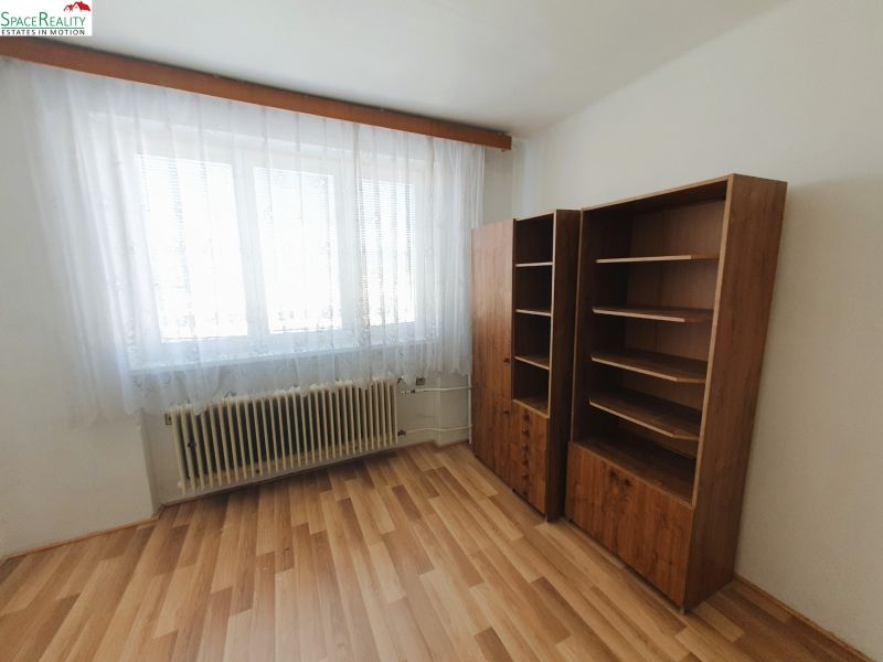 A room with a wooden decor floor in a 3-room apartment, two shelves, a radiator.