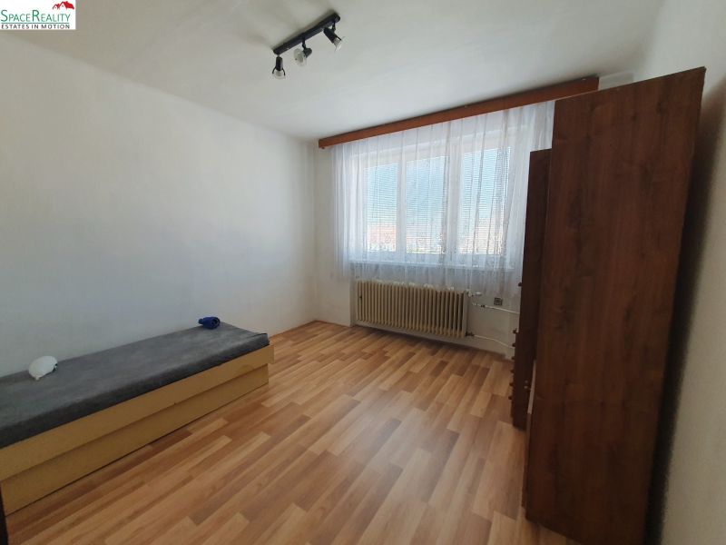 A bedroom in a three-room apartment with a wooden decor floor and simple furnishings.