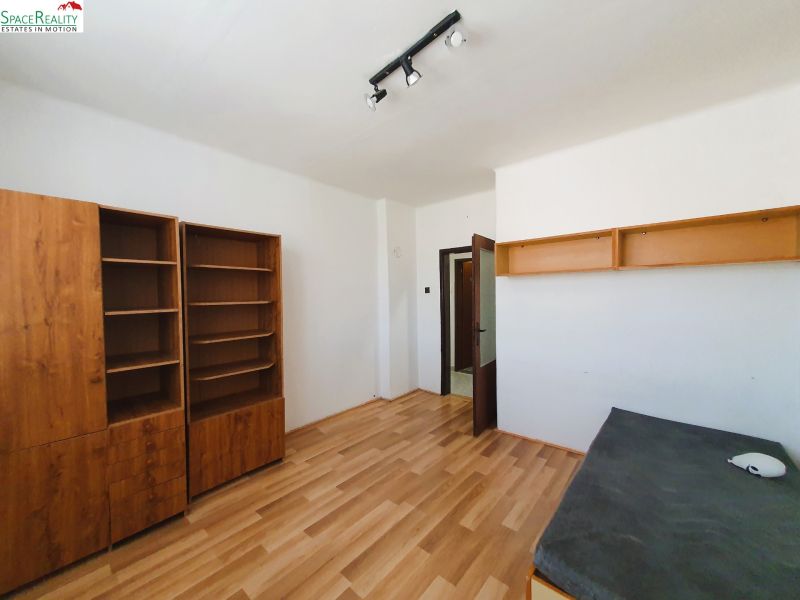 A room in a 3-room apartment with a wooden decor floor and a shelving unit.