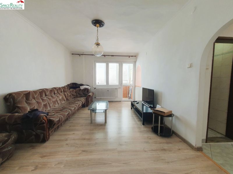 Living room with a brown sofa, television, and wood-patterned flooring in a three-room apartment.