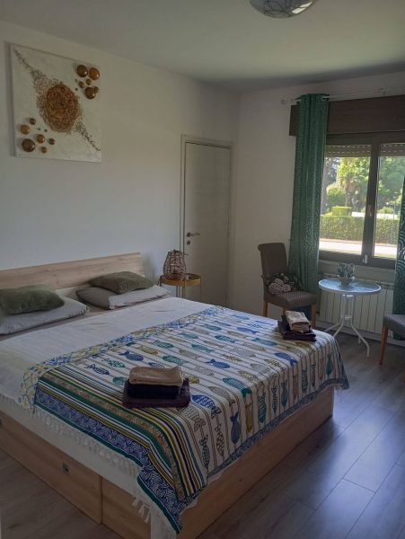 Bedroom in a holiday apartment with wood-patterned flooring, colorful throw, and an armchair.