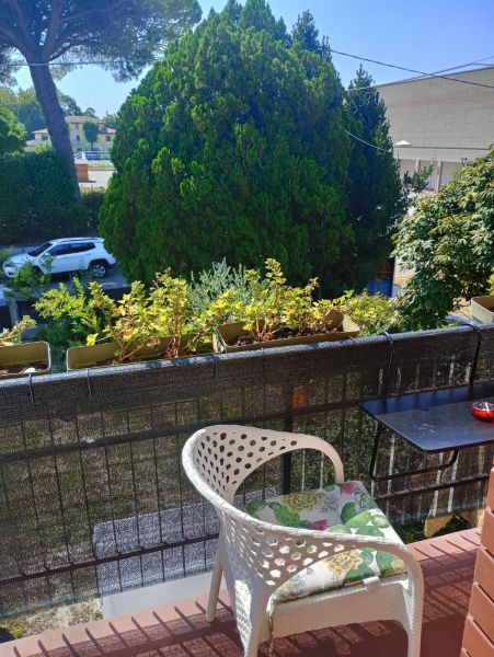 The balcony of a holiday apartment in Bibione with a comfortable chair and a view of greenery.