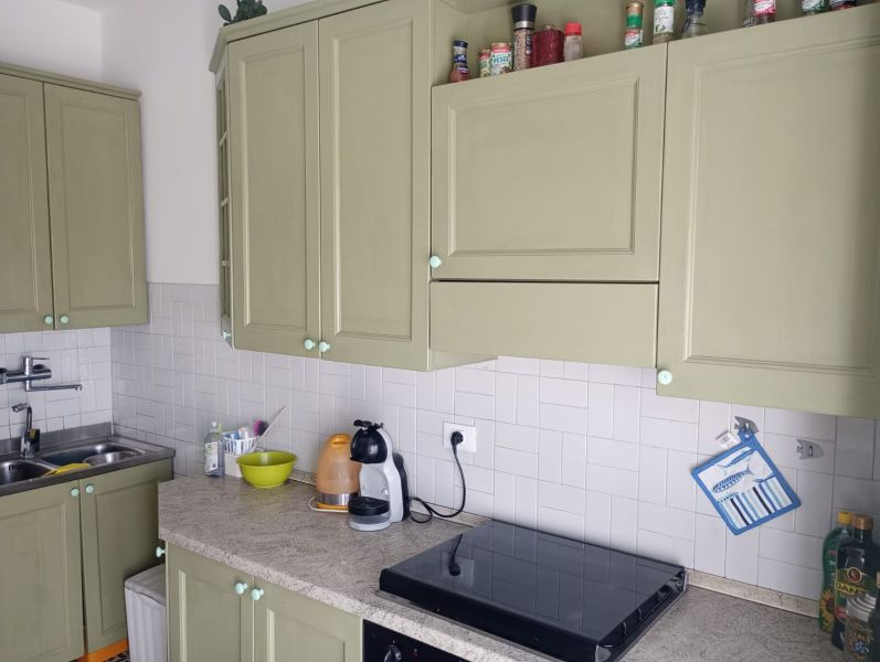 A kitchen in a holiday apartment with white tiles and green cabinets.