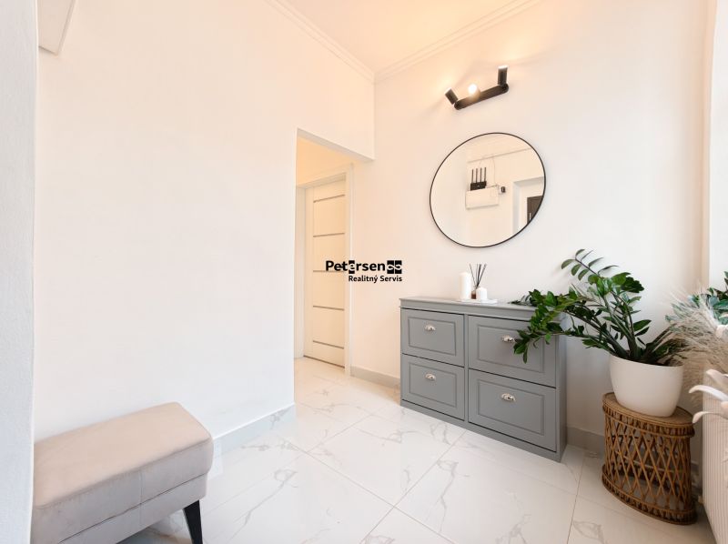A bright hallway in a 3-room apartment with white walls, a green plant, and a dresser.