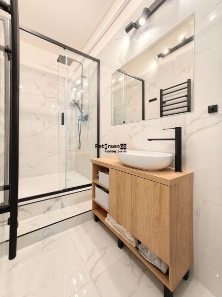 A bathroom in a 3-room apartment with a shower corner and a cabinet with a wooden decor.