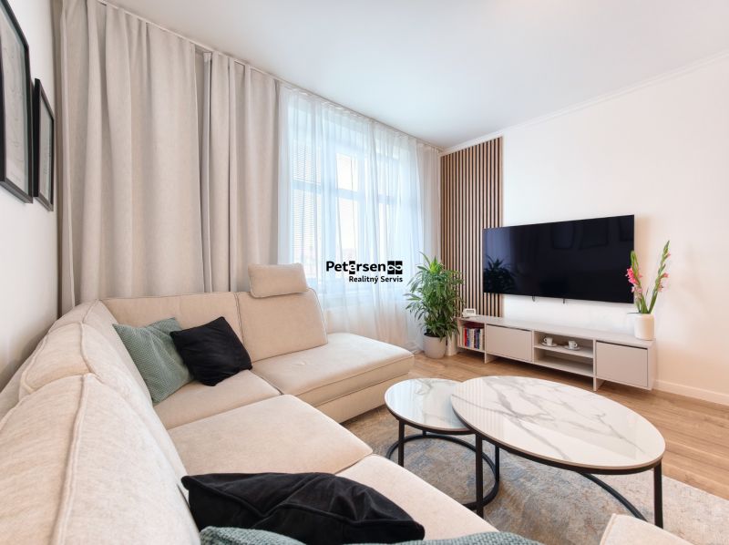 Living room of a three-room apartment with a sofa, table, and TV on a floor with a wooden decor.