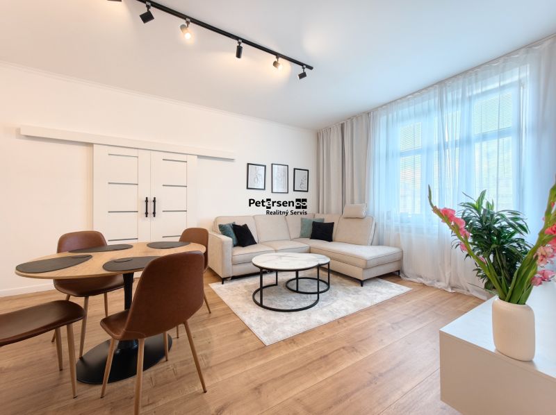 Living room in a three-room apartment with a sofa, dining table, and wooden decor flooring.