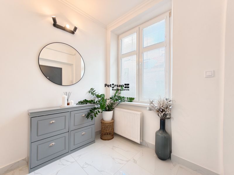 Duplex interior with a window, green plants, and a gray dresser in a 3-room apartment.