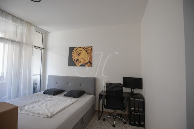 A bedroom with a single bed, a desk, and a picture above the bed in a two-room apartment.