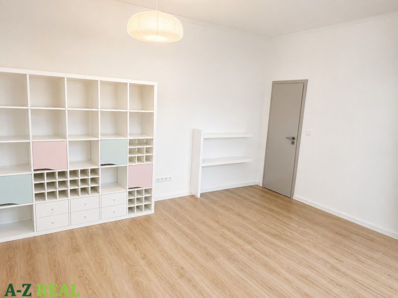 A room in a 3-room apartment with a wooden decor floor and a white shelf.