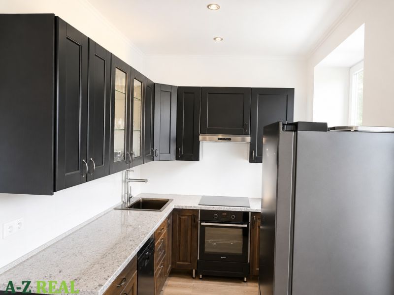 A kitchen in a 3-room apartment with black cabinets, white walls, and a granite countertop.