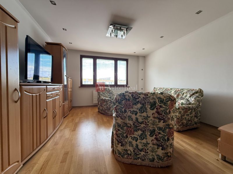 Living room in a 4-room apartment with a floral sofa and wooden decor flooring.