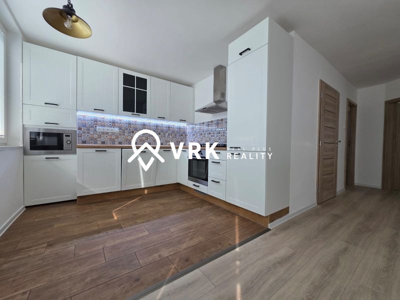 A kitchen in a 3-room apartment with a wood-patterned floor and white cabinets.