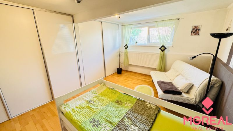 A bedroom in a family house with a wooden decor floor, a sofa, and a built-in wardrobe.