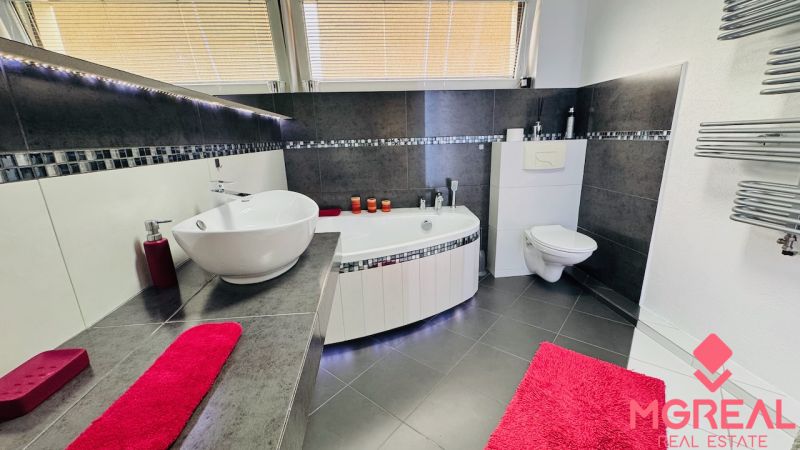 A bathroom in a family house with a bathtub, a sink, and tiles with a dark design.