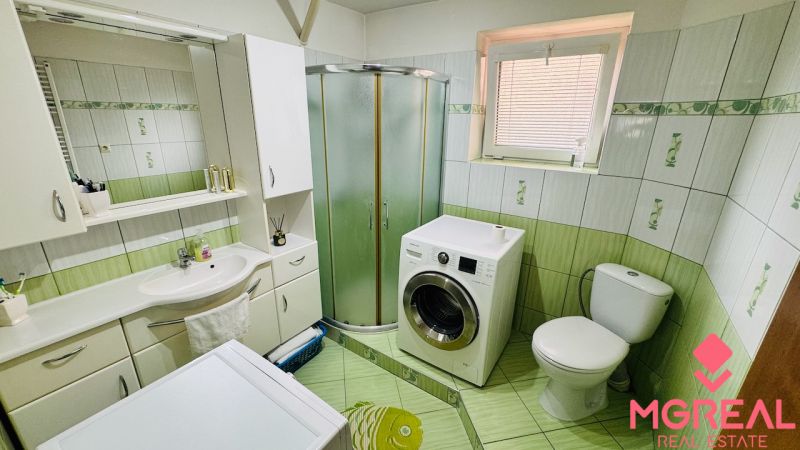 A bathroom in a family house with a washing machine, shower, and green tiles.