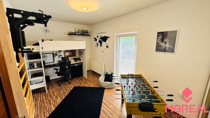 A room with a bunk bed and a foosball table, floor with wood decor.