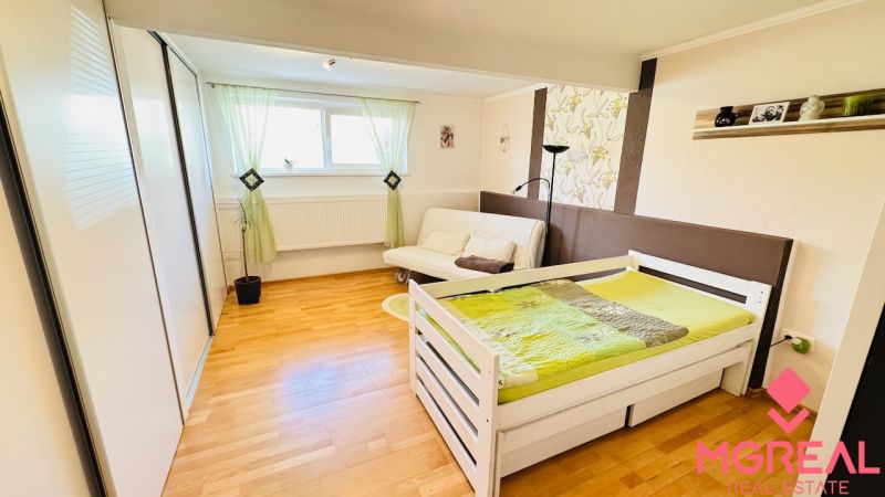 A bedroom in a family house with a bed, a sofa, and a wooden decor floor.