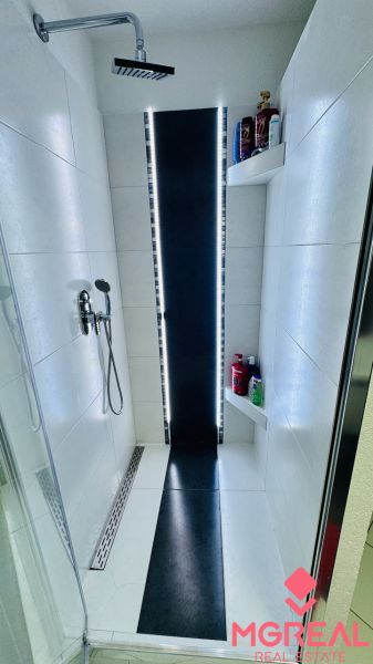 Shower enclosure with LED lighting and shelves in the bathroom of a family house.
