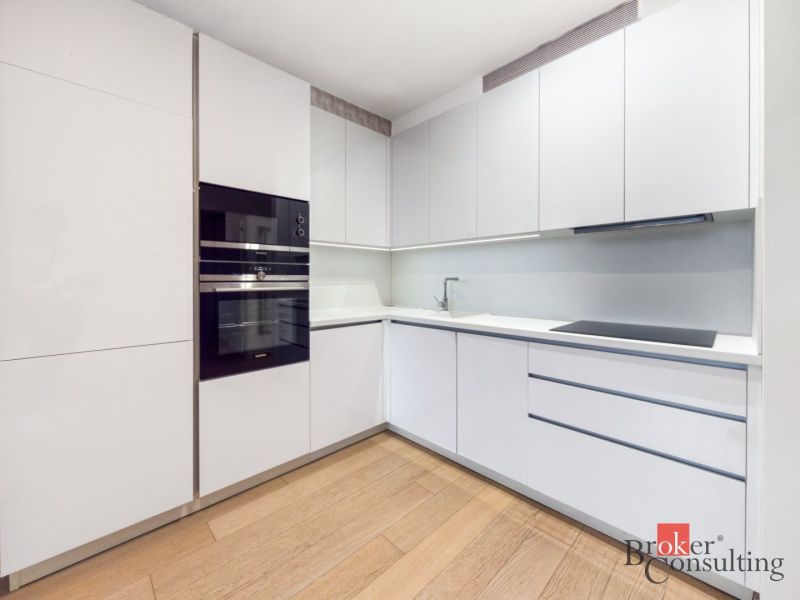 A kitchen with white cabinets and a wood-patterned floor in a two-room apartment.