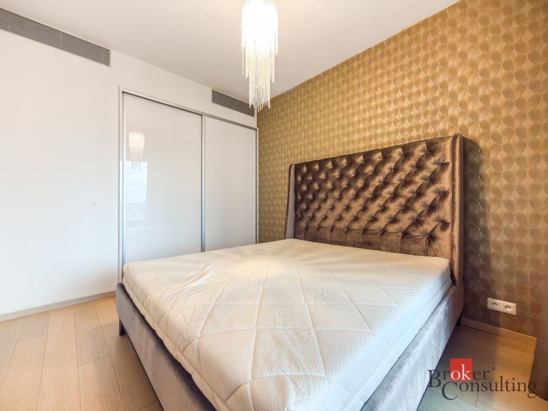 A bedroom in a two-room apartment with an upholstered bed and wallpapered walls.