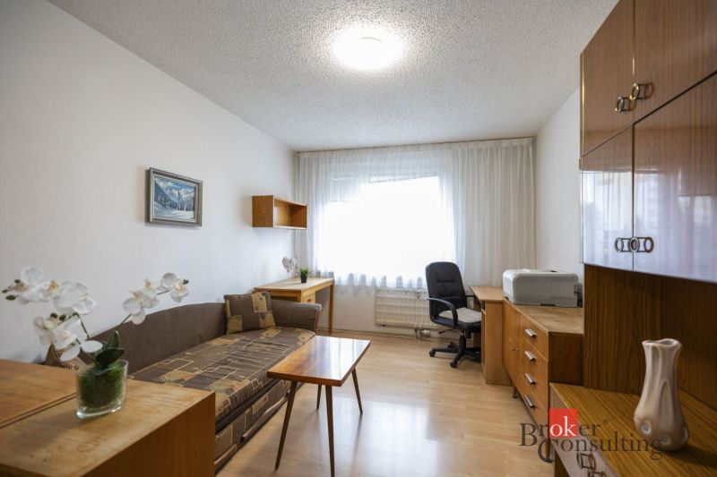 Living room with a sofa, office chair, and wooden-patterned flooring in a 4-room apartment.