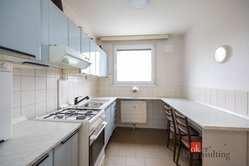 A kitchen with a gas stove and wooden chairs in a 4-room apartment.