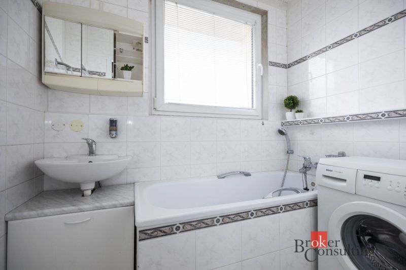 Bathroom with a mirror, bathtub, and washing machine in a 4-room apartment. White tiles with a pattern.