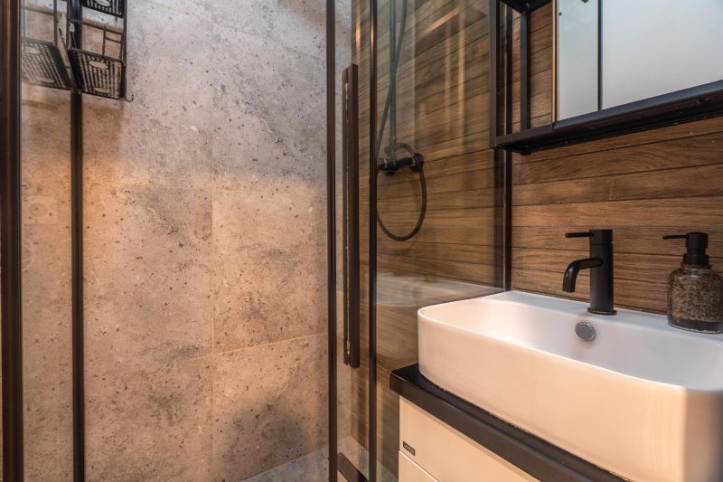 A bathroom with a sink, dark fixtures, and walls in natural stone and wood decor.