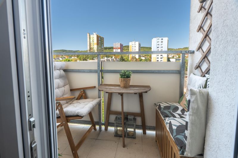A balcony with a view of the housing estate, wooden furniture, and greenery. Bratislava - Rača, Sadmelijská.