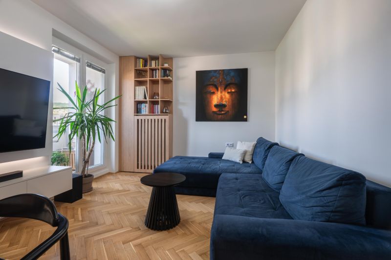 Living room with a blue sofa, painting, bookshelf, and wooden decor flooring in a three-room apartment.