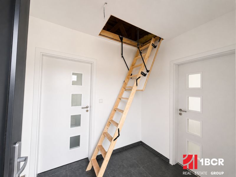 The interior of a family house with a foldable staircase to the attic and white doors.