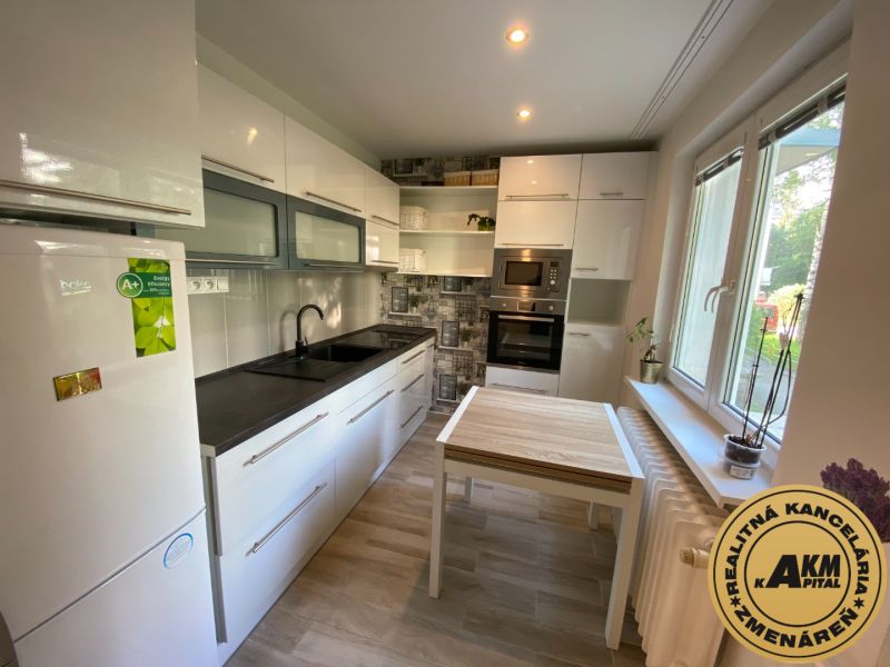 A bright kitchen with white cabinets and a table that has a wood-patterned floor.