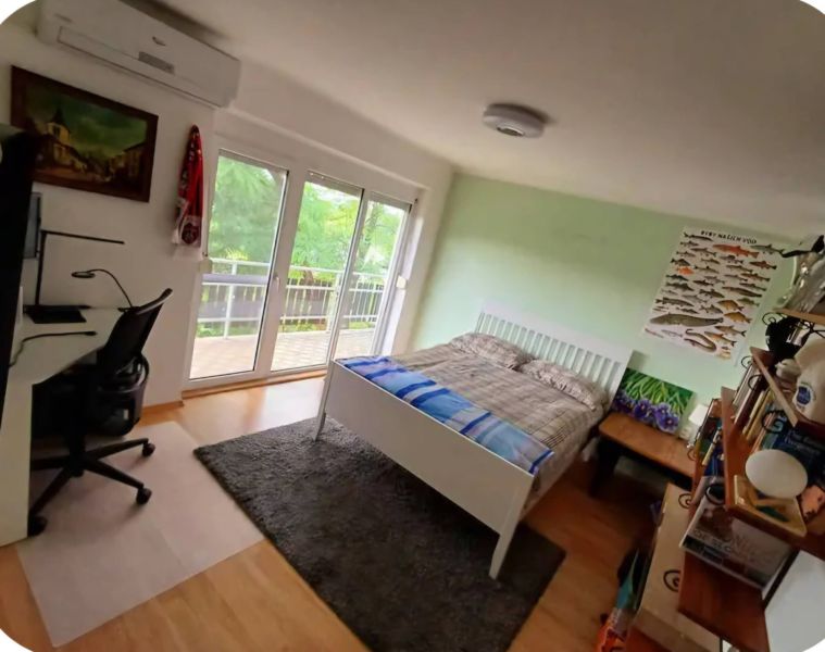 Bedroom in a family house with a bed, a desk, and a wooden decor floor.