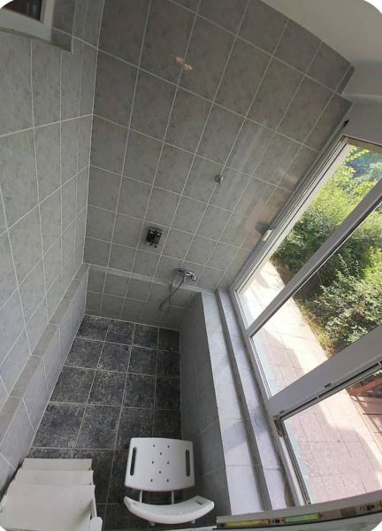 A shower corner with tiles and a shower chair in a family house.