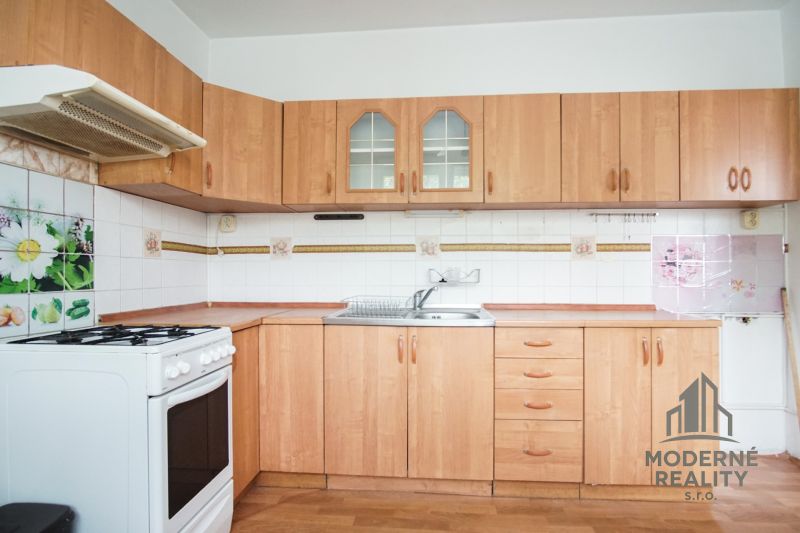 A kitchen with light furniture and a wooden decor floor in a 3-room apartment.