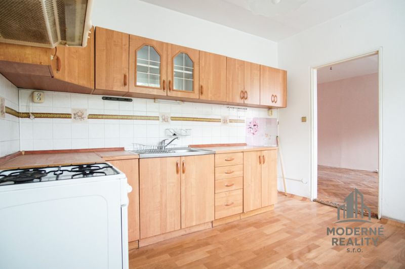 A kitchen in a 3-room apartment with a light-colored kitchen unit and a floor with a wood design.