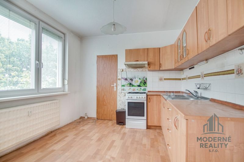 A kitchen in a 3-room apartment with a wooden floor decor and a view of greenery.