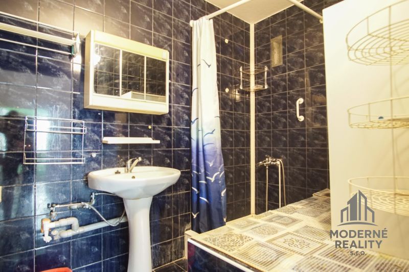 A bathroom in a 3-room apartment with dark tiles and a shower corner.