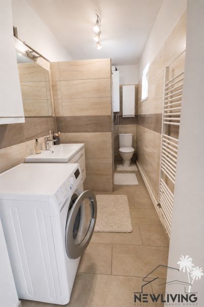 A bathroom in a family house with a washing machine, sink, shower, and toilet, with a wooden decor floor.