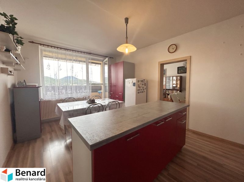 A kitchen in a three-room apartment with a wooden decor floor and red cabinets.