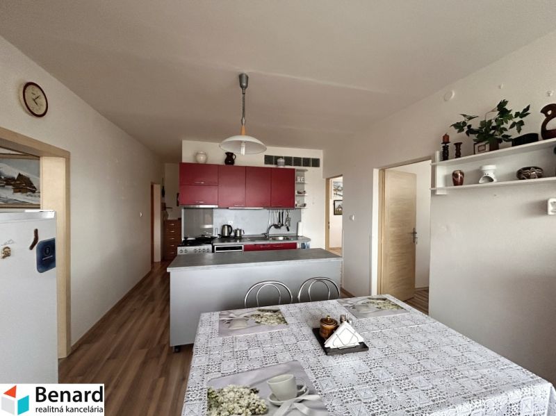 A kitchen in a 3-room apartment with a table, red cabinets, and a floor with a wood decor.