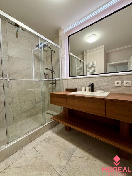 The bathroom of a two-room apartment with a spacious shower and a sink on a wooden cabinet.