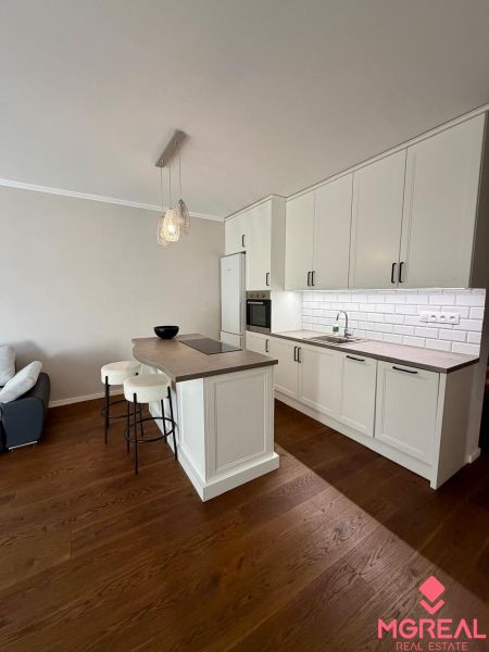 A kitchen in a 2-room apartment with an island, white cabinets, and a wood-patterned floor.