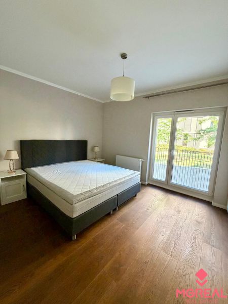 Bedroom in a 2-room apartment with a bed, a lamp, and a wooden decor floor.