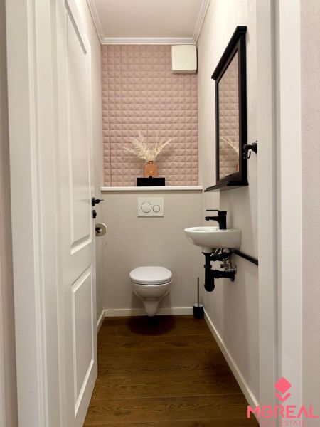 A toilet with a wall featuring a geometric pattern, a mirror, and a floor with a wooden decor.