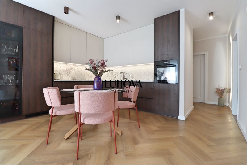 A kitchen in a 3-room apartment with a wood-patterned floor and pink chairs.